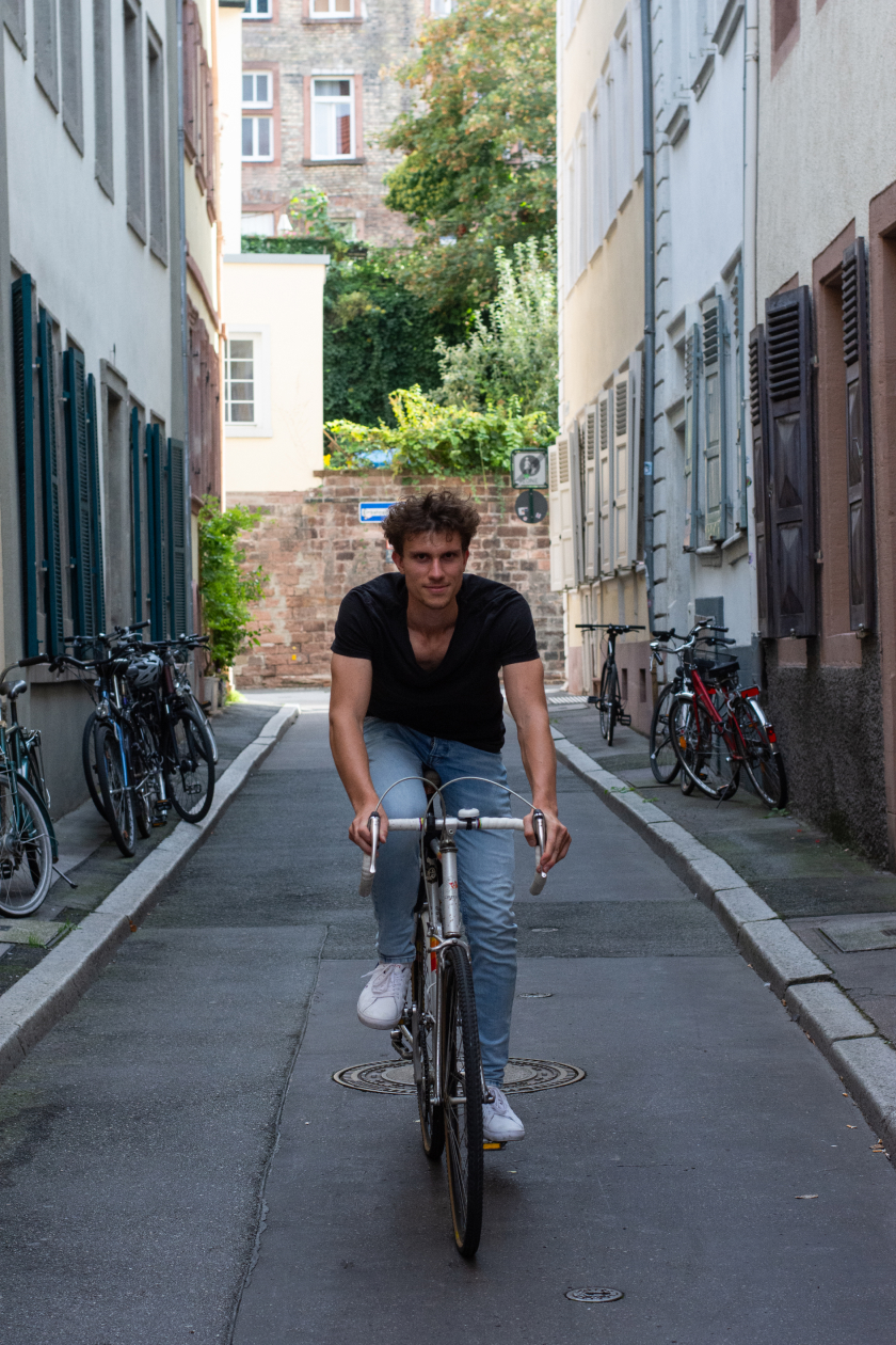 Philipp lächelnd auf einem Fahrrad in einer sehr schönen Gasse, diesmal mehr im Bildvordergrund
